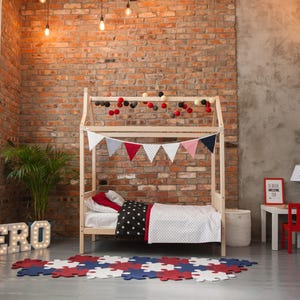 Natural solid wood toddler bed frame with removable rails set up in a brick wall nursery interior.