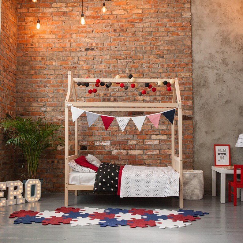 Natural solid wood toddler bed frame with removable rails set up in a brick wall nursery interior.