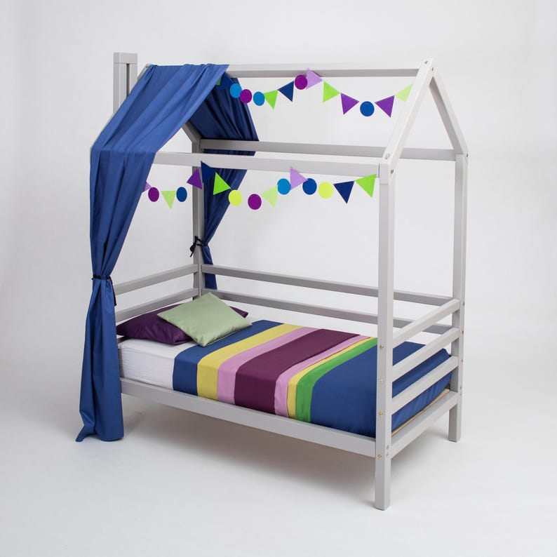 White solid wood toddler house bed frame with removable rails and navy blue canopy drapes for parents.