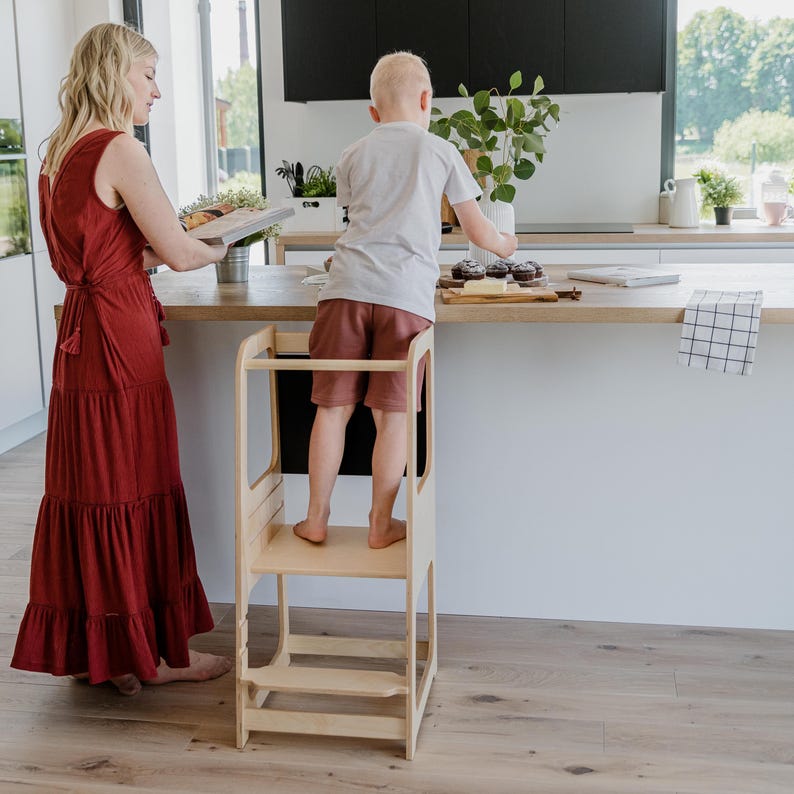 Mother watching her young boy stand on a 3-level height adjustable stool while assisting with afternoon lunch prep.