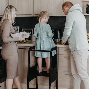 Parents baking pastries with their toddler standing on a black child cooking step stool, resolving morning routine chaos.