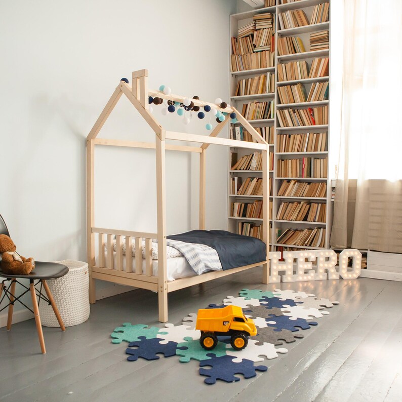 Natural wood cabin bed on legs in a cozy child nursery next to a full bookcase and toy construction trucks.