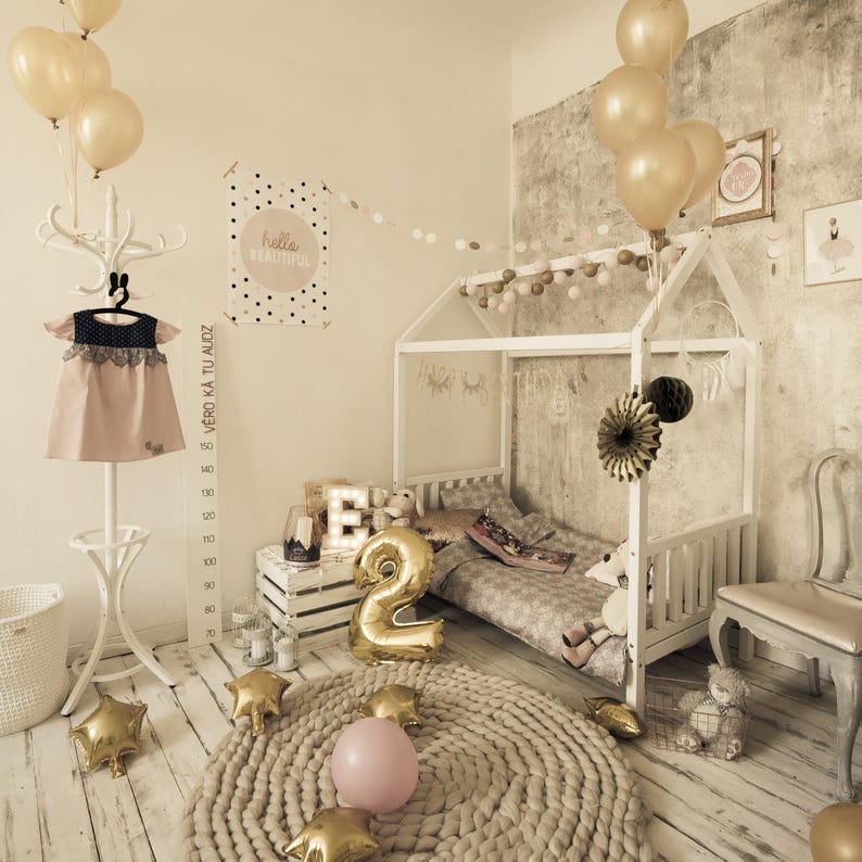 Natural solid wood canopy bed decorated with pastel drapes and balloons for a toddler girl bedroom.