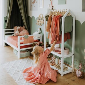 Child easily reaching dresses on a low wooden garment stand to build self-care skills