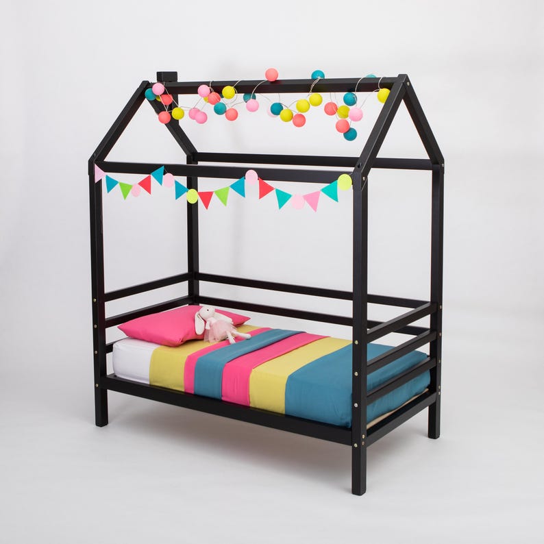 Black solid wood Montessori house bed frame decorated with colorful garlands and birch plywood slats.