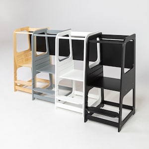 Pode incluir: Quatro torres de aprendizagem em madeira dispostas em fila, com acabamentos em madeira natural, cinzento, branco e preto. Cada torre inclui uma plataforma, uma barra de segurança e um degrau inferior, com um painel traseiro que serve de lousa.