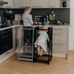 Two young girls standing on grey and black kitchen step stools, eliminating chair climbing during baking activities.