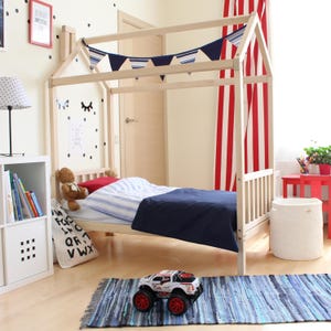 Natural solid wood canopy bed frame on legs with blue bedding set up in a bright child bedroom.