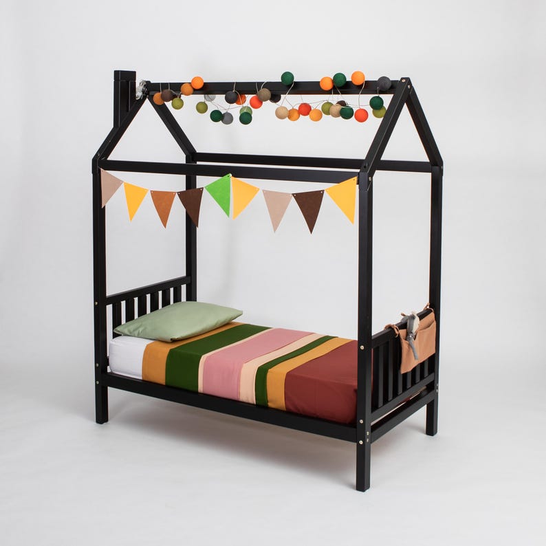 Black solid wood cabin bed on legs with removable guard rails and colorful bunting garland.