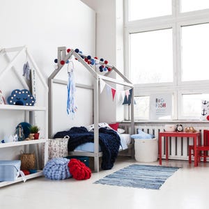 Wide-angle shot of a minimalist Montessori kids room featuring a modern house bed frame on legs with ample natural window light.