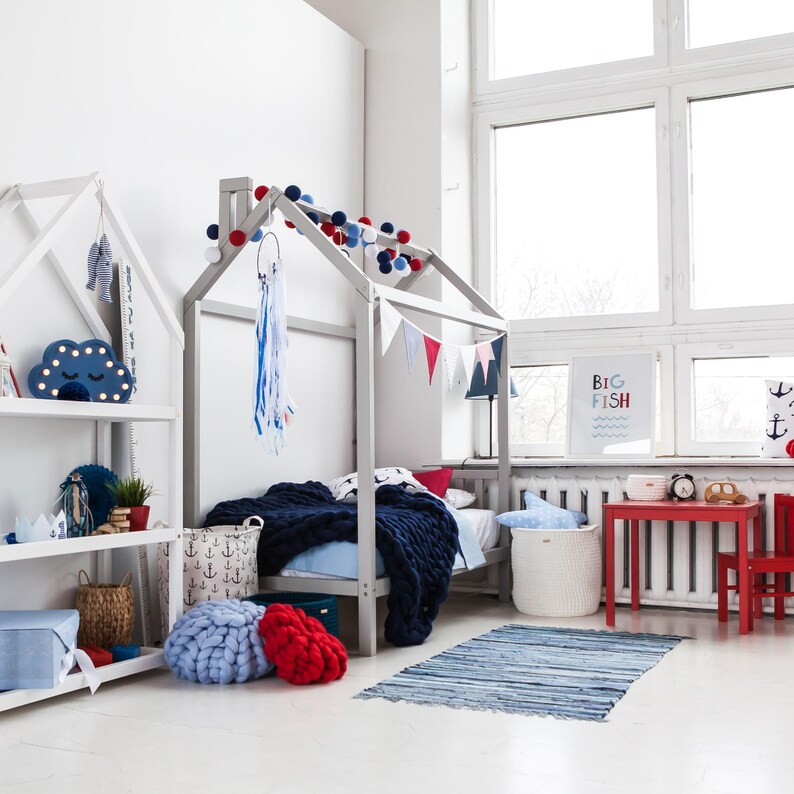 Wide-angle shot of a minimalist Montessori kids room featuring a modern house bed frame on legs with ample natural window light.