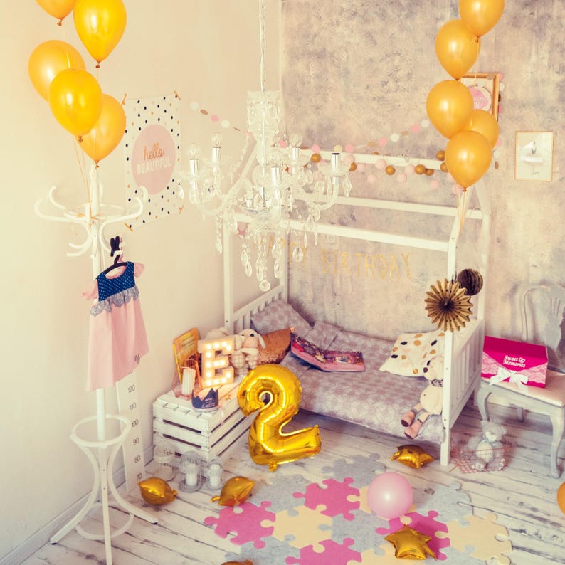 Natural solid wood toddler house bed decorated with balloons and pink drapes for a girl bedroom.