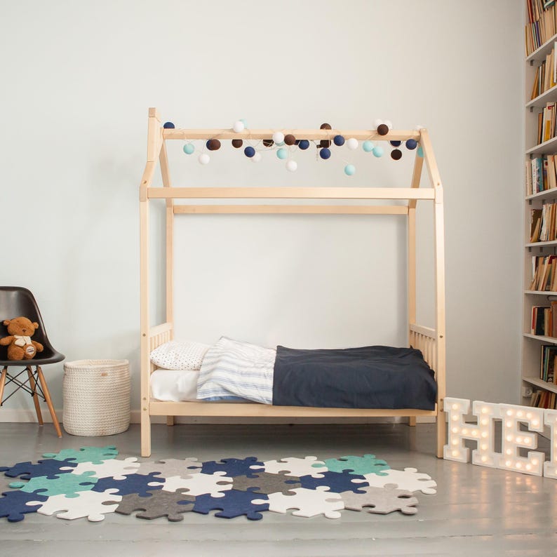 Natural solid wood daybed frame on legs with blue bedding displayed in a brightly lit child room.