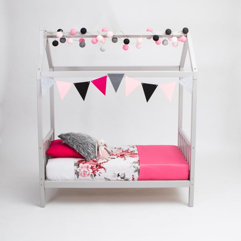 Grey solid wood daybed frame with removable safety guard rails and soft pink drapes for toddlers.