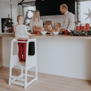 White grow-with-me step stool positioned in a holiday decorated kitchen, giving grandparents a charming Christmas gift idea.