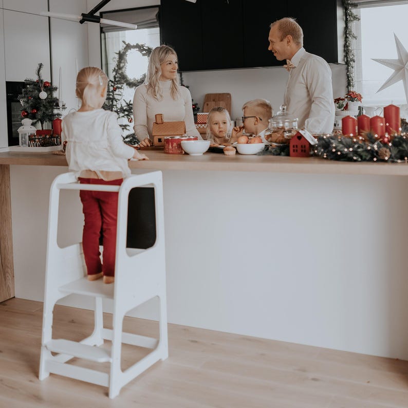 White grow-with-me step stool positioned in a holiday decorated kitchen, giving grandparents a charming Christmas gift idea.