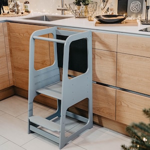 Grey child standing tower with a blackboard panel set near oak cabinets, offering sleek modern nursery organization.