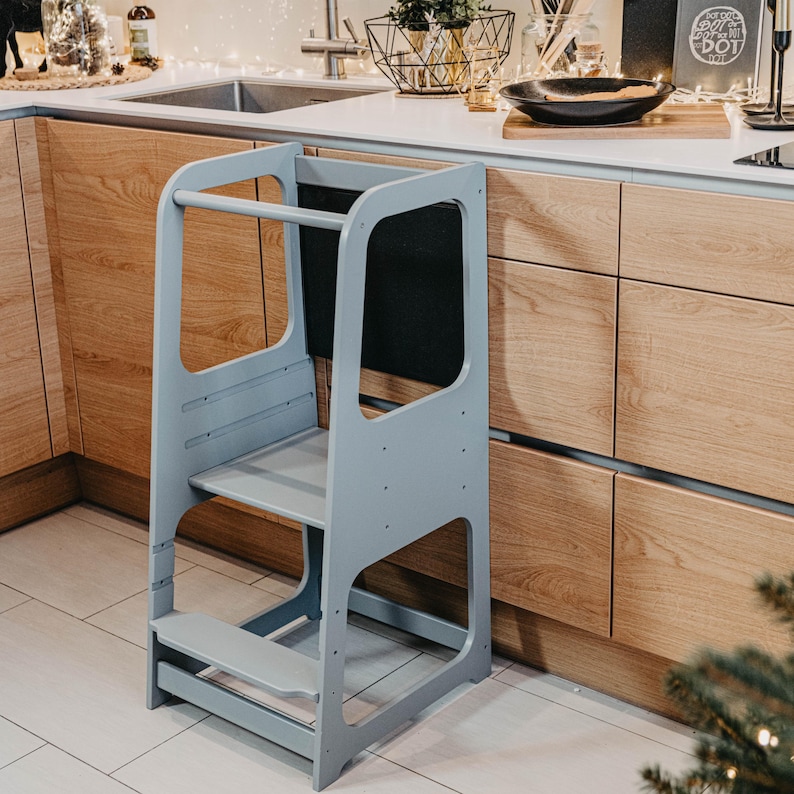 Grey child standing tower with a blackboard panel set near oak cabinets, offering sleek modern nursery organization.