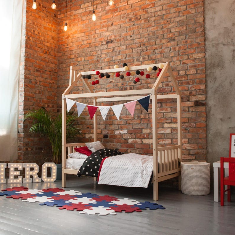 Natural solid wood platform house bed with removable safety rails in a modern brick wall nursery.