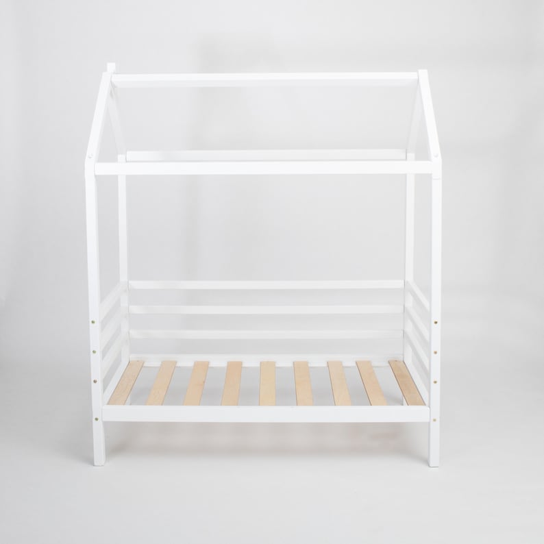 White solid wood Montessori house bed frame on legs with visible birch plywood mattress support slats.