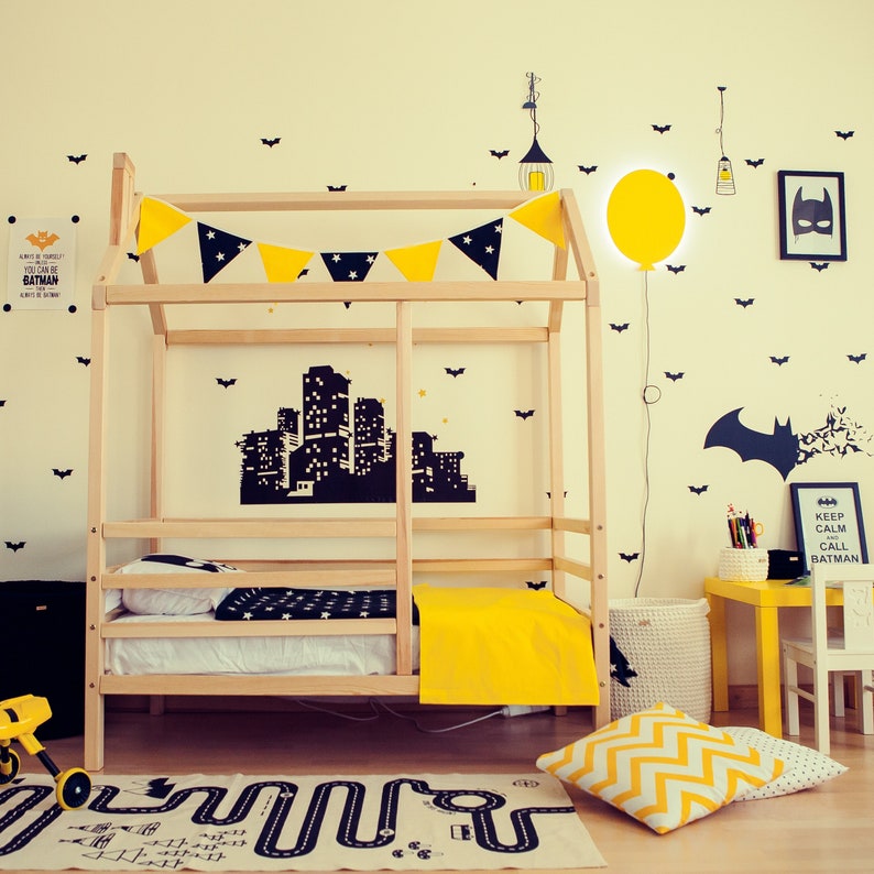 Puede incluir: Una cama de madera con una colcha de estampado amarillo y negro. La cama est&aacute; decorada con siluetas de murci&eacute;lagos negros y una pegatina de una ciudad. Una l&aacute;mpara de globo amarillo cuelga de la pared. El letrero sobre la cama dice "Keep Calm and Call Batman".