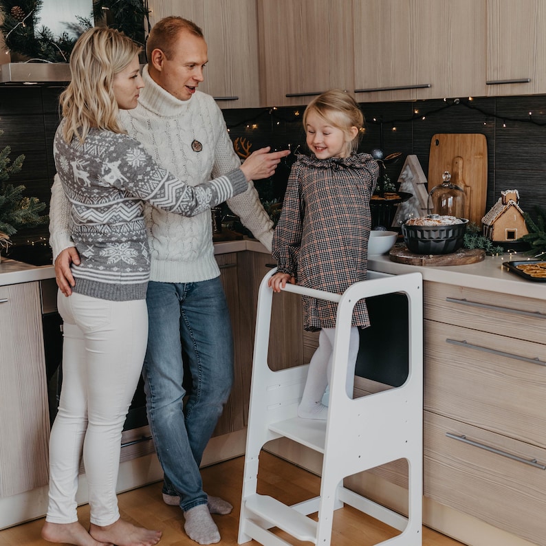 Family gathering around a white 3-level height adjustable stool in the kitchen, giving godparents a thoughtful present idea.