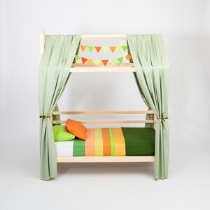 Natural solid wood toddler bed on legs featuring removable safety rails and green canopy drapes.