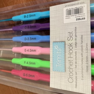 Pu&ograve; includere: Un set di sei uncinetti in una confezione di plastica trasparente. Gli uncinetti sono codificati a colori e etichettati con dimensioni da 2,5 mm a 5,0 mm. La confezione &egrave; etichettata "Crochet Hook Set" e "Trimits".