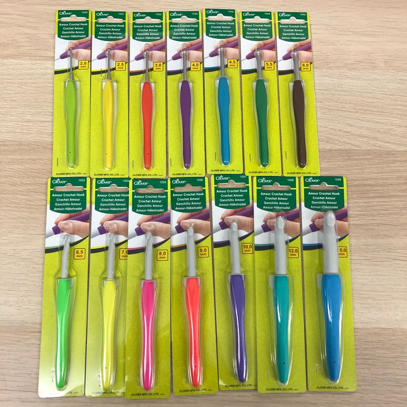 May include: A set of 14 colourful crochet hooks, individually packaged on green and white cards. The hooks are labelled with their size in millimetres. The hooks are arranged in two rows, with the smaller hooks in the top row and the larger hooks in the bottom row.