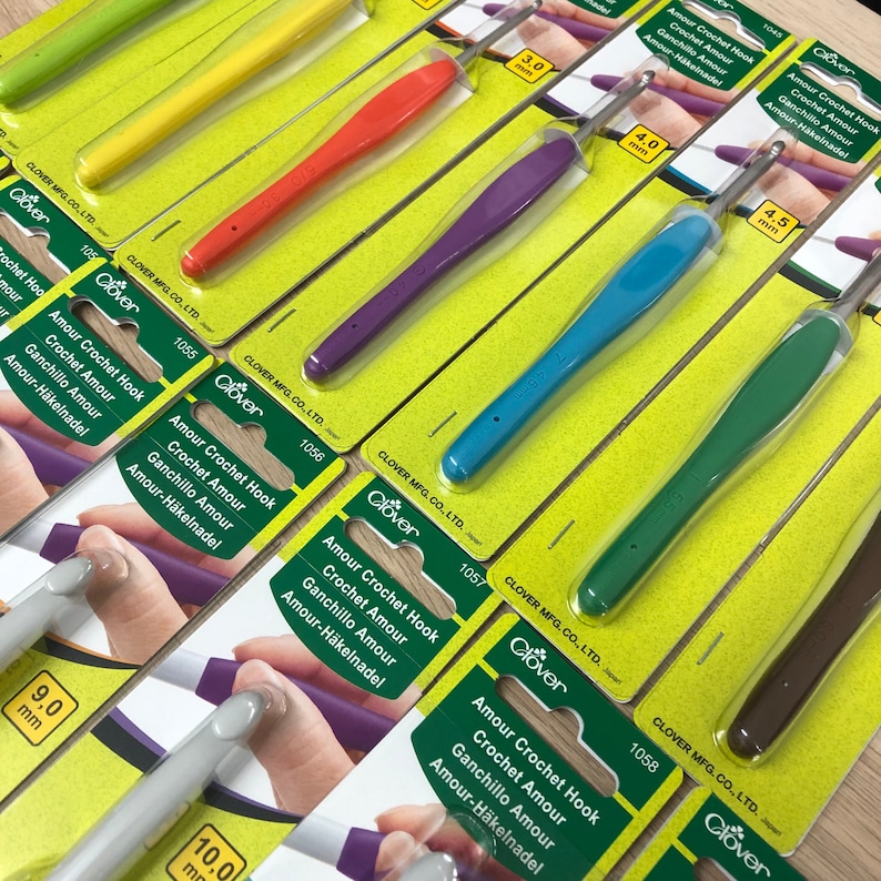May include: A set of nine Clover Amour crochet hooks in various sizes, ranging from 3.0 mm to 10.0 mm. The hooks are individually packaged on green and yellow cards with the Clover logo and product information.