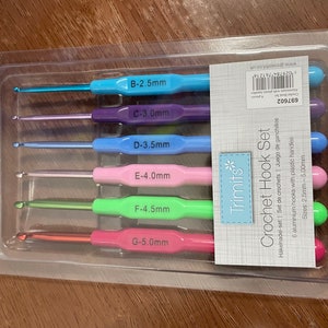 Pu&ograve; includere: Un set di sei uncinetti in una confezione di plastica trasparente. Gli uncinetti sono codificati a colori e etichettati con dimensioni da 2,5 mm a 5,0 mm. La confezione &egrave; etichettata "Trimits* Crochet Hook Set" e include il testo "6 uncinetti in alluminio con manici in plastica".