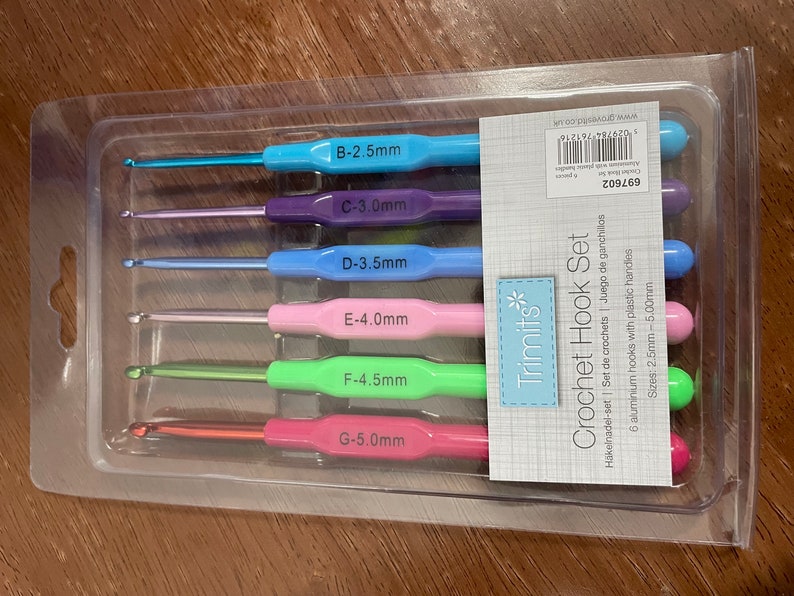 Pu&ograve; includere: Un set di sei uncinetti in una confezione di plastica trasparente. Gli uncinetti sono codificati a colori e etichettati con dimensioni da 2,5 mm a 5,0 mm. La confezione &egrave; etichettata "Trimits* Crochet Hook Set" e include il testo "6 uncinetti in alluminio con manici in plastica".
