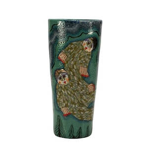 May include: A tall, hand-painted ceramic vase with a teal and dark blue background. The vase features two figures in patterned clothing. The figures have red accents and are set against a backdrop of stylized trees.