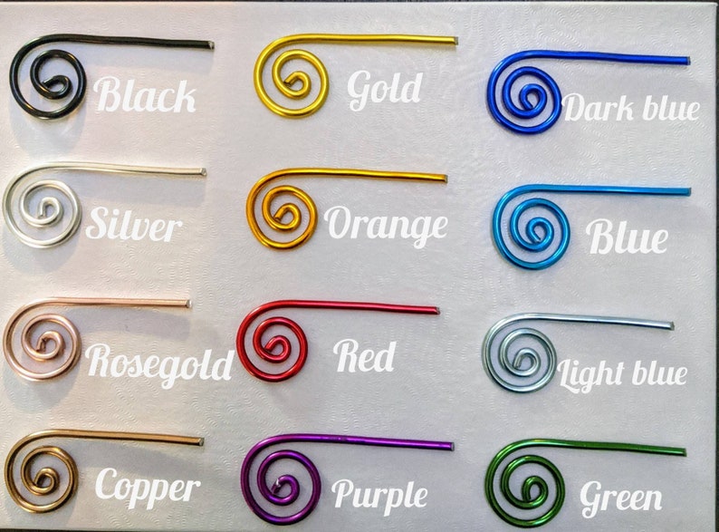 May include: A collection of twelve spiral-shaped wire clips arranged in a grid. Each clip is a different color with its corresponding name printed next to it: Black, Gold, Dark blue, Silver, Orange, Blue, Rosegold, Red, Light blue, Copper, Purple, and Green.