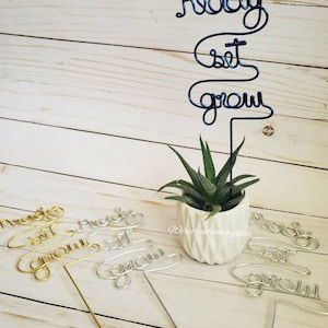 May include: A set of three wire plant markers with the words "Ready Set Grow" in different colors. The markers are made of wire and are designed to be inserted into the soil of a plant. The markers are a fun and decorative way to add a touch of personality to your plants.
