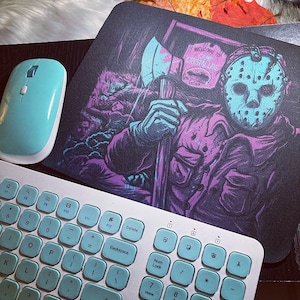 May include: A mouse pad with a graphic of a hockey mask-wearing figure holding an axe. The figure is standing in front of a sign that reads "Welcome to Camp Crystal Lake".
