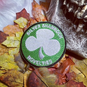 May include: A green and white embroidered patch with a shamrock design. The patch reads "Silver Shamrock Novelties".
