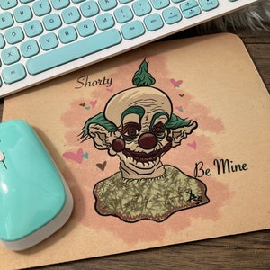 May include: A brown mouse pad with a cartoon illustration of a creepy clown with green hair and a red nose. The clown is wearing a green and brown sweater and the text "Shorty" and "Be Mine" are written on the mouse pad.