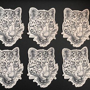 May include: Six black and white leopard head illustrations on a black background. Each illustration is a sticker with a white border.