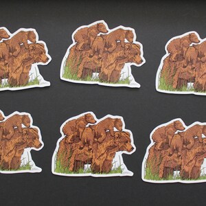 May include: Six stickers featuring a brown bear with two cubs stacked on top. The bears are depicted in a detailed illustration style, with green grass at the base. The stickers have a white border and are arranged on a black surface.