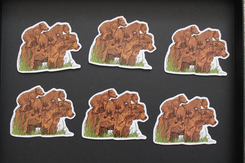 May include: Six stickers featuring a brown bear with two cubs stacked on top. The bears are depicted in a detailed illustration style, with green grass at the base. The stickers have a white border and are arranged on a black surface.