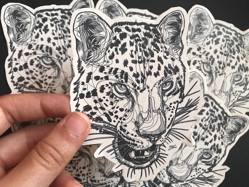May include: A set of black and white line art stickers featuring a close-up of a leopard's face. The stickers are printed on white paper and have a glossy finish.