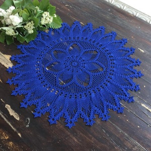 Peut inclure: Une nappe ronde en crochet bleu avec un motif floral délicat. La nappe a un bord festonné.