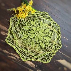 Puede incluir: Un encaje de ganchillo verde con un diseño floral. El encaje está sobre una superficie de madera.