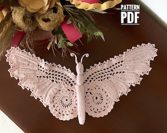 Peut inclure: Un délicat papillon en crochet rose avec des détails complexes. Le papillon est posé sur une surface en bois brun foncé. Le texte "PATTERN PDF" est visible dans le coin supérieur droit de l'image.