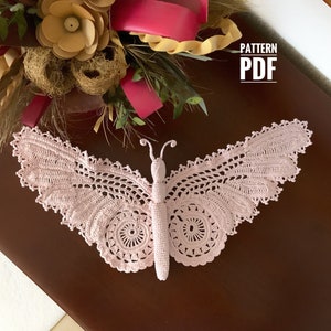 May include: A delicate pink crocheted butterfly with intricate details. The butterfly is laying on a dark brown wooden surface. The text "PATTERN PDF" is visible in the upper right corner of the image.
