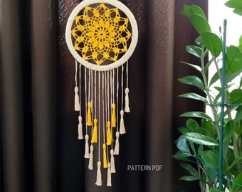 May include: A white crocheted dreamcatcher with yellow tassels hanging from it. The dreamcatcher is hanging in front of a brown curtain. The text "PATTERN PDF" is visible in the bottom right corner of the image.