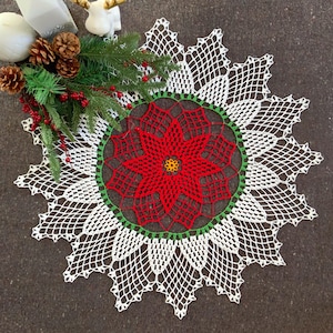 May include: White crochet doily with a red poinsettia design in the centre. The doily has a scalloped edge and is perfect for adding a touch of festive cheer to your home decor.
