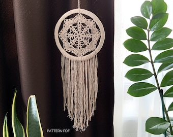 May include: A white crocheted dream catcher with a geometric pattern and fringe hanging from a brown curtain. The text "PATTERN PDF" is visible in the bottom left corner of the image.