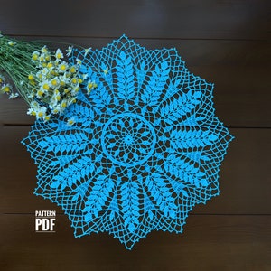 Op de afbeelding: Een blauwe gehaakte doily met een bladmotief. De doily ligt op een houten oppervlak. PATTERN PDF